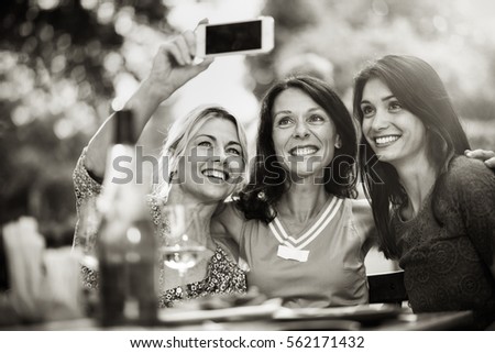 Group of female friends in their thirties taking a selfie during a party on a terrace. In the background a beautiful garden where their men doing a bbq. Black and white