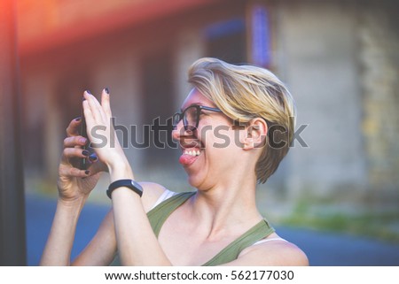 Portrait of beautiful girl with blond hair with the phone in his hand, young woman making selfie, the woman Hamming and showing tongue.