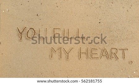 Handwriting words "YOU FILL MY HEART" on sand of beach