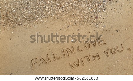 Handwriting words "FALL IN LOVE WITH YOU" on sand of beach