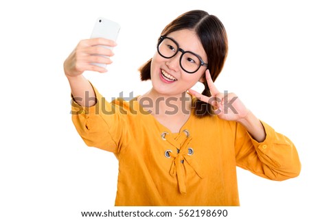 Young happy Asian woman smiling while taking selfie picture with mobile phone and giving peace sign