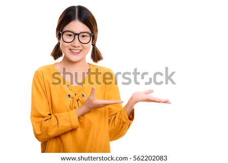 Studio shot of young happy Asian woman smiling while showing something