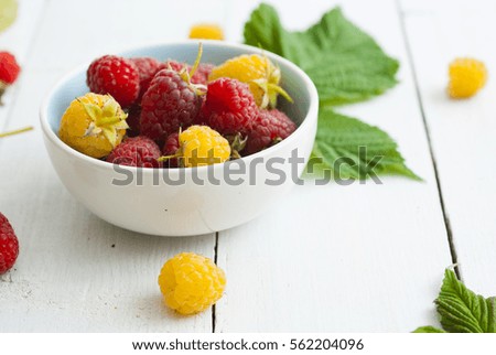 red and rare yellow raspberry fruits on white wooden table background