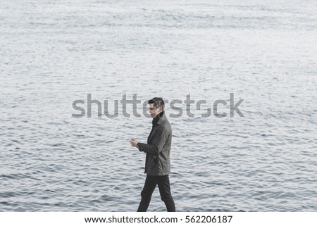 handsome young man in coat walking near water