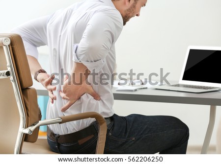 Young man suffering from backache in office, closeup Royalty-Free Stock Photo #562206250