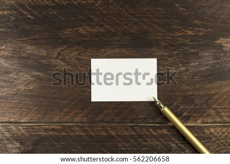 A square photo of a blank white thick cardboard business card on a dark wooden background texture with a golden ink pen. A mockup or a minimalist banner with copyspace