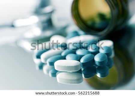 closeup of the desk of a doctors office with a bottle with pills in the foreground and a stethoscope in the background Royalty-Free Stock Photo #562215688