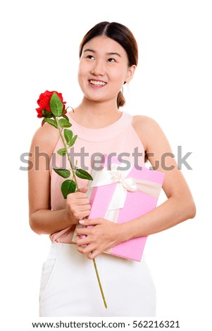 Young happy Asian woman smiling and thinking while holding red rose and gift box ready for Valentine's Day