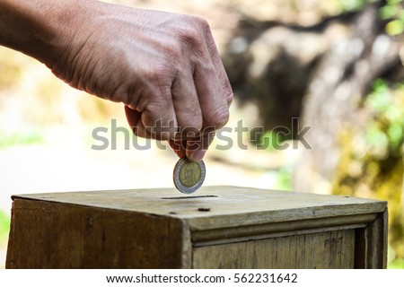 A man hand putting coin into a wooden box as donation Royalty-Free Stock Photo #562231642