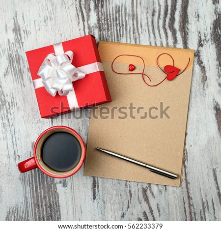 Red coffee cup, empty notepad with pen and two red hearts on wooden surface, with heart cookies. Valentines day concept.