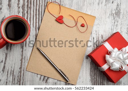 Red coffee cup, empty notepad with pen and two red hearts on wooden surface, with heart cookies. Valentines day concept.