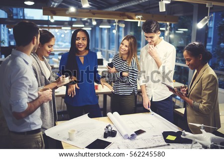 Studying group of male and female designers working in friendly atmosphere creating map of city landscape under orders from skilled leader using wireless connection to internet and modern technologies Royalty-Free Stock Photo #562245580