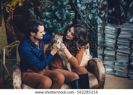 beautiful couple in love with a cat in their arms sitting on the sofa, hugging, smiling and kissing. Family concept