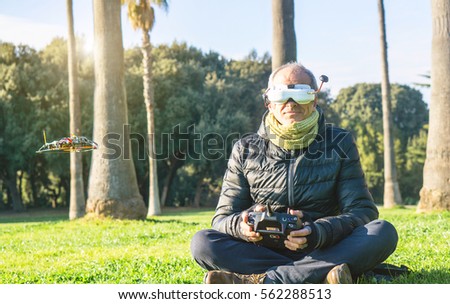 Senior man having fun with new technologies of flying drones wearing virtual reality glasses - Adult piloting his racer drone built by himself with remote control -  First person view