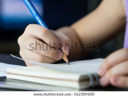 Child hand is using pencil to practice writing on a book. Kid learning to write letter on to a paper, For pre school education concept. Royalty-Free Stock Photo #562309600
