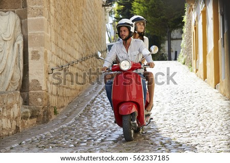 Couple riding motor scooter in old Ibiza street, full length Royalty-Free Stock Photo #562337185