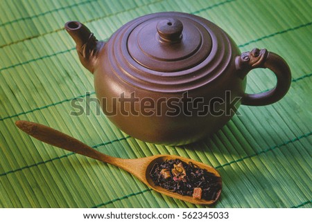 Close-up ceramic teapot and  dried tea in wooden spoon on  green bamboo background.