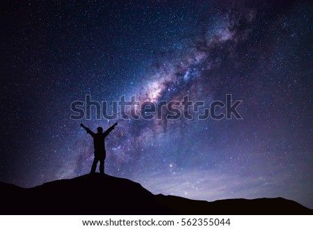 Milky Way landscape. Silhouette of Happy man standing on top of mountain with night sky and bright star on background.  Royalty-Free Stock Photo #562355044