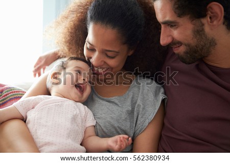 Parents Sitting On Sofa Cuddling Baby Daughter At Home Royalty-Free Stock Photo #562380934