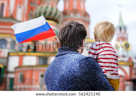 Little boy and his middle age father holding russian flag with Saint Basil's Cathedral on background 
