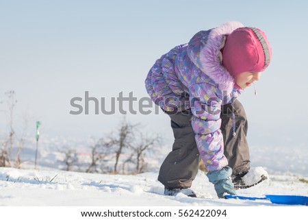 Cute girl in winter snow playground with sleds outdoors