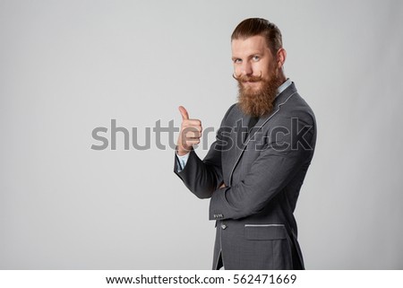 Confident stylish business man in suit standing with folded hands gesturing thumb up, over grey background Royalty-Free Stock Photo #562471669