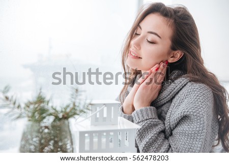 Picture of beautiful young lady dressed in sweater sitting in cafe at cold winter day. Eyes closed.