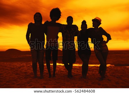 Group of men and women arm in arm at beach on sunset