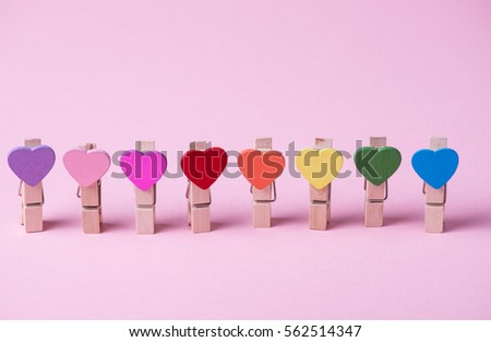 Colored heart shaped clothespins in row on pink background