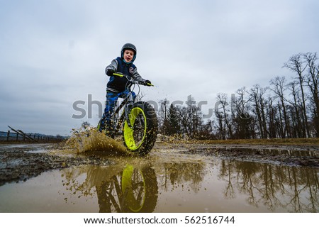Young boy smiling as he is riding his fat bike through the mud puddles on a rainy and cloudy day.