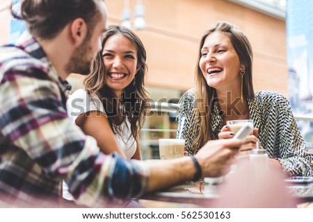 Multiracial group of friends having a coffee together. Two women and a man at cafe, talking, laughing and enjoying their time. Lifestyle and friendship concepts with real people models. Royalty-Free Stock Photo #562530163