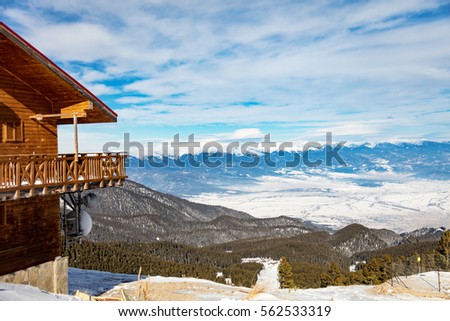 Panorama view of a ski slope and wooden house at mountain covered snow.