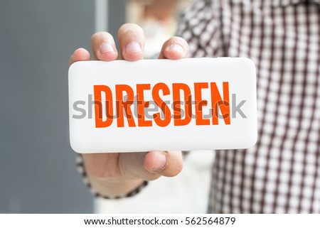 Man hand showing DRESDEN word phone with  blur business man wearing plaid shirt.