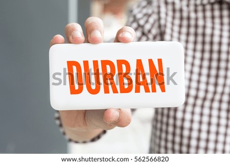 Man hand showing DURBAN word phone with  blur business man wearing plaid shirt.