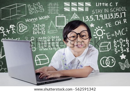 Cute little student using laptop computer while smiling at camera with scribble background on the blackboard