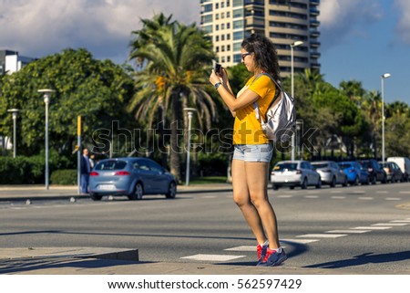 Young and sporty woman is standing next to the road and taking a picture of it on sunny day, Barcelona, Spain