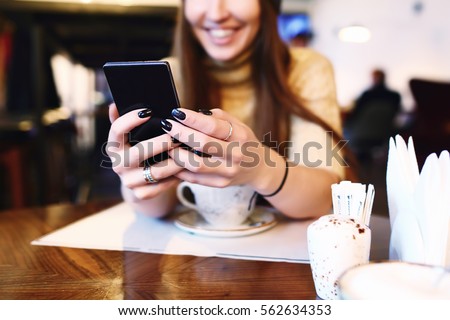 Close up of women's hands holding cell telephone with blank copy space scree for your advertising text message or promotional content, hipster girl watching video on mobile phone during coffee break Royalty-Free Stock Photo #562634353