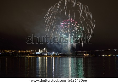 Beautiful firework on night sky in tromsoe city with bridge, cathedral and colorful reflection on the cold fjord water surface. Delayed new years eve firework due to weather, launched in january 2017