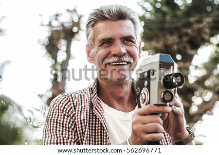 Vintage photography is his passion. Shot of a handsome senior man taking a picture with a vintage camera outdoor.