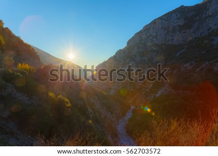 Setting sun above hills with path leading through the gorge in Greece