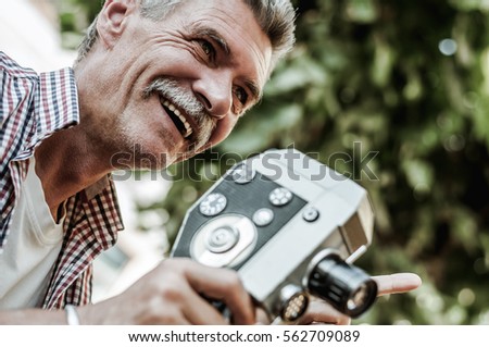 He looks at life from all angles.Close up shot of a persistent senior man using an old video camera for his investigation while walking on the park.