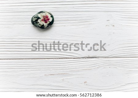 Small painted pebble close-up, romance story or childhood memory concept, oval rock with flower drawing, st. valentines day present, space for text, love concept, white wood background