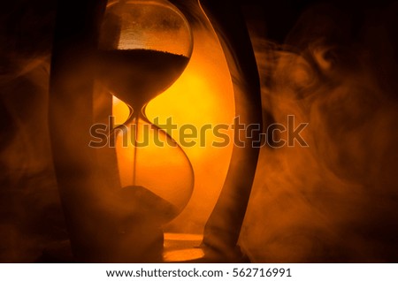 Time concept. Silhouette of Hourglass clock and smoke on dark background with hot yellow orange red blue cold back lighting, or symbols of time with copy space, sandglass or sand clock
