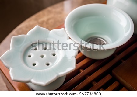 Modern ceramic Chinese tea set - closeup of tea bag rester and strainer on traditional wooden tray. The rester is shaped in a lotus flower design.