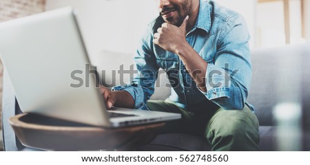 Smiling bearded African man working at home while sitting on the sofa.Concept of young people using mobile devices.Blurred background.Cropped Royalty-Free Stock Photo #562748560