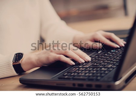 Closeup view young businesswoman working at a laptop, typing on keyboard while sitting her work place.Horizontal,color filter, blurred background