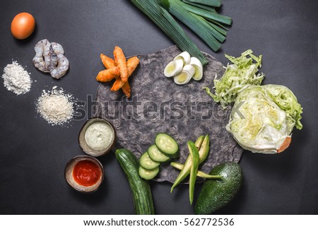 Top view ingredients for pita sandwich with raw, grill tiger shrimp, cabbage, leek, cucumber, avocado, vegetable, egg, meal, spicy sauce and mayonnaise, black bread over black grunge background.