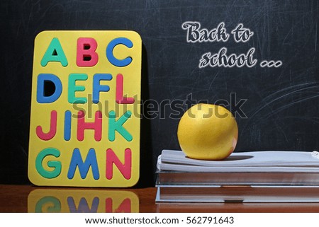 Still life with school books and apple against blackboard with "back to school" on background