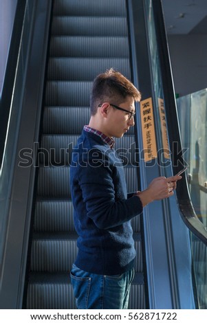 Asian handsome young man standing in front of  an escalator using a smart phone