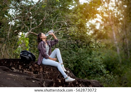 A young beautiful woman with backpack is drinking water the hot sun, on the mountain.